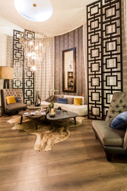 Casa Cor Bolívia 2015: Lobby por Maya Mc Lean - Maya se inspirou em um hotel boutique para criar um ambiente de estilo moderno, quente, com materiais naturais, como madeiras entalhadas, texturas, couros e acabamentos nas cores cinza e café. A iluminação escolhida é quente, com lustres e candeiros. Nas paredes, revestimentos de madeira e papel de parede texturizado de pele de anaconda, que combina com o tapete de couro.