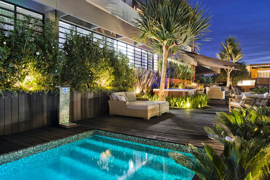 Jardim da Piscina - Nadia Bentz, Vanderlan Farias e Beto Lemos. As medidas do espaço, de aproximadamente 35 m de comprimento por 5 m de largura, foram um desafio. Para suavizar essa extensão e o formato irregular da área, os profissionais buscaram verticalizar ao máximo possível, utilizando plantas altas. O verde exuberante é potencializado no contraste com os acabamentos de tons escuros. Um dos pontos de destaque é a piscina em fibra, com acabamento de pastilhas de vidro.