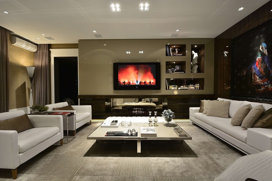 FHF 40 Living - Francisco Humberto Franck. Neste estar, bastaram 36m² para criar um ambiente multiúso, para ver TV, receber amigos ou relaxar. Móveis baixinhos, com um estilo anos 1970, e detalhes em cimento queimado nos revestimentos dão o tom informal. Eles ganham a companhia elegante dos painéis amadeirados com alto brilho, dos espelhos facetados bronze e dos mármores aplicados no piso e na lareira.
