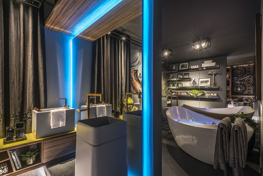 Suíte do Casal Ciclista: Bárbara Falqueto e Carolina Lage.A sala de banho com hidromassagem fica mais reservada graças à divisória espelhada, contornada com a fita de LED azul. O par de cubas diferentes individualiza o espaço de cada um. No reflexo do espelho é possível ver parte do armário, que exibe bicicletas e acessórios, tendo como fundo a parede revestida com OCA.
