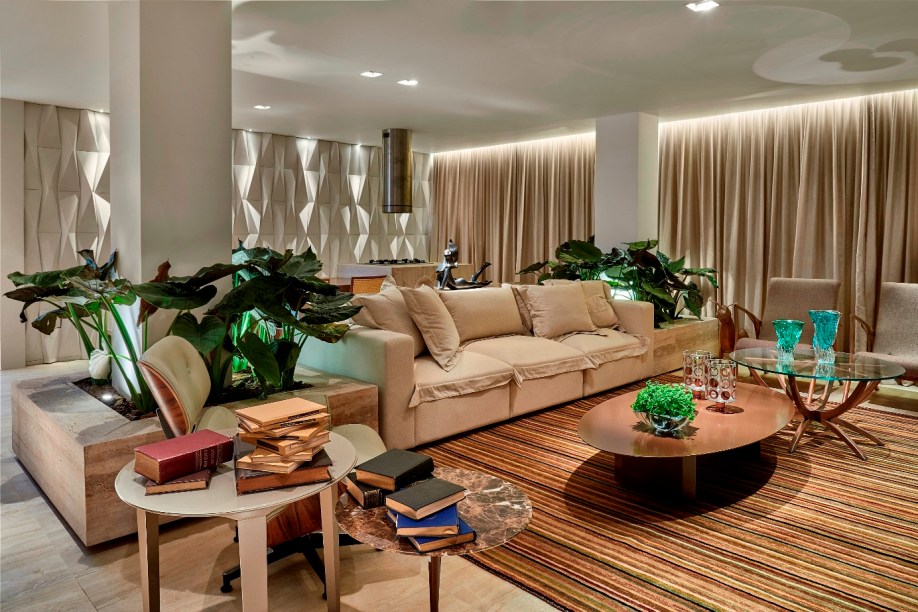 Family Room - Miguel Gustavo. O visitante é impactado pela combinação de materiais com a iluminação especial direcionada, que se dilui nas cortinas ou no revestimento 3D na parede de fundo do espaço gourmet integrado. Tons neutros e naturais aquecem o projeto, que traz cores pontuais nos objetos decorativos e nas plantas e pedras tipicamente brasileiras.
