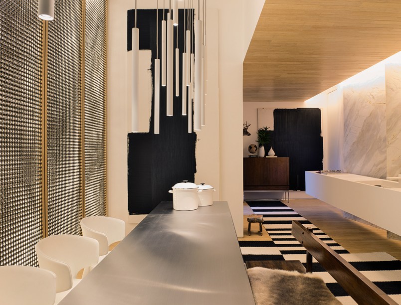 Cozinha Gourmet Todeschini - Guilherme Torres. A bancada em Corian soluciona o espaço ao funcionar como armário e ao ocultar a pia e a máquina de lavar. A mesa em inox inova com o sistema de cocção por indução, que dispensa o uso de fogão e confere o visual adequado ao espaço que é um híbrido de cozinha e estar. O duo preto e branco é explorado de várias formas, transmitindo um ar futuristas.