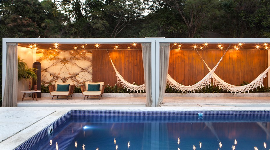 Largo das Águas - Ana Dieuzeide, André Victor de M. Alves, Laila Santos. A praça central da CASA COR abrange 370m², setorizados em piscina, varanda, deck, espelho d’água, galeria, palco e jardins. Um sistema de módulos do tipo contêineres organiza os espaços - e alguns recebem um telhado verde para amenizar a temperatura. O granito e a madeira foram instalados por meio de encaixes para possibilitar a reutilização posterior ao evento. O painel desenvolvido por Gustavo Rodrigues evoca o tema da brasilidade e reforça o clima de varanda trazido pelas redes.