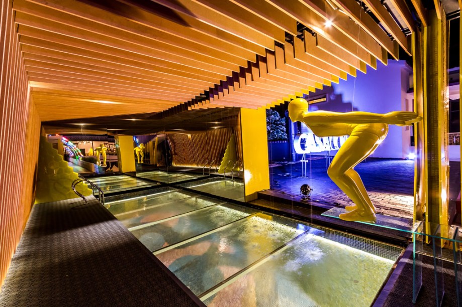 Casa Cor Bolívia 2015: Agua Bendita por Oscar Anglarill e José María Navarra - A dupla se encarregou do espaço pouco conhecido pelo público: a piscina do colégio. Por isso, eles o transformaram num lugar chamativo. A cerâmica, original da época, foi coberta com vidro, dando a sensação de que a piscina está cheia de água. Na fachada, ainda há vidros hexagonais na cor amarela.