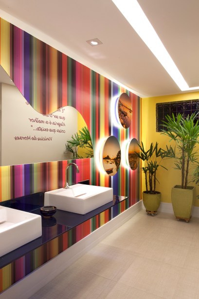 Lavabo Funcional Feminino - Raquel Mello. A profissional fugiu dos azulejos, pisos e louças brancas para mostrar a alegria das cores na parede principal. O espelho tem as formas sinuosas do Pão de Açúcar, e a bancada é um cubo de vidro azul como o mar. A abertura feita na parede amarela garante a ventilação natural.