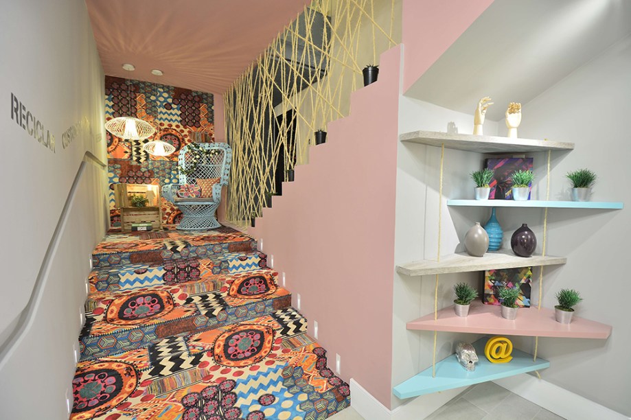 Atelier da Céu – Camila Pigato, Fernanda Sá e Laura Tavares. A escada é revestida em tecido estampado e tem guarda-corpo de cordas de sisal. No alto, a cadeira vintage marca o cantinho da inspiração. Outro detalhe interessante são as prateleiras cuja disposição foge do ângulo reto.