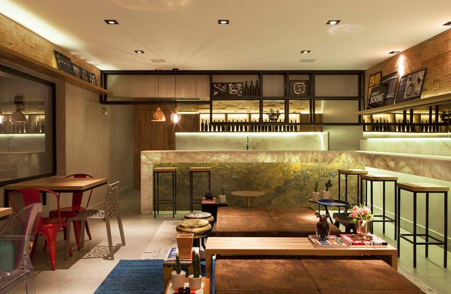 Lounge Bar - Mariah Cardoso. Metais, cimento e ferro oxidado afirmam o contraste entre estruturas rígidas e obras de arte de cores suaves. A ideia era lançar um olhar diferente sobre materiais crus e urbanos em um ambiente flexível e descomplicado, que também utiliza cimento queimado, latão, mármores nobres e peças garimpadas em sucatas. As pedras brutas são destaque, convertidas em elementos decorativos através da iluminação.