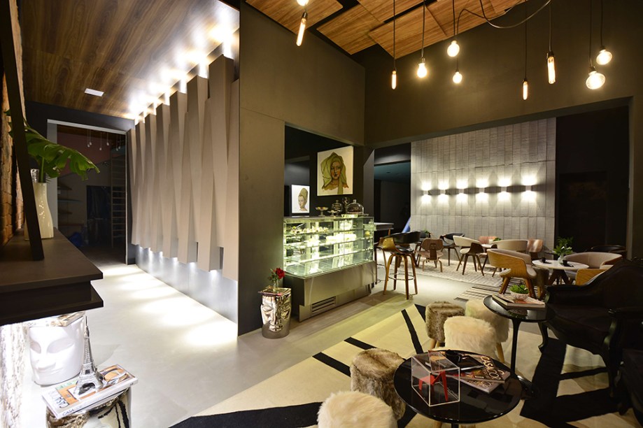 Café do Clube - Carla Oliveira e Ricardo Cavichioni. Mesas e cadeiras são todas diferentes, mas com uma leitura semelhante que preserva a harmonia. Placas de concreto ou esculturas 3D em MDF são aliadas à iluminação e criam efeitos nas paredes. No teto, placas em madeira parecem flutuar e dão suporte aos pendentes.