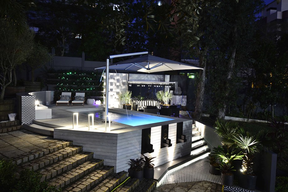 Espaço Água e Fogo – Piscina Igui - Carla Michele Zignani, Andreia Rossato e Rafael Artico. Fogo e água, preto e branco são alguns opostos que se atraem no projeto, que se beneficia dos desníveis do terreno para criar pequenos ambientes de estar. Na área da piscina, destaque para o banco em quartzo branco. Nos revestimentos, cimentícios e porcelanatos são combinados à madeira pinus do deck, finalizado com tinta esmalte branca. Ao fundo, a parede verde foi composta de mini cicas e iluminação com pontos de LED na cor verde.