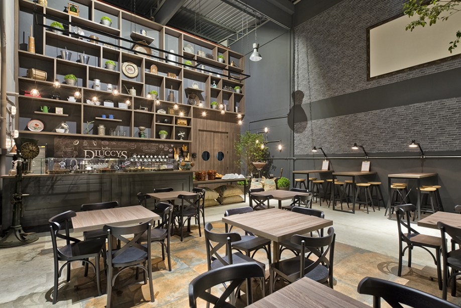 Café - Viviane Tabalipa. O espaço aproveitou imagens das primeiras edições d’O Estado do Paraná, locado onde eram as rotativas do jornal. O que também levou a arquiteta a trabalhar com um estilo mais industrial, mantendo a estrutura aparente de telhado, luminárias existentes e piso em concreto, intercalado com o porcelanato em aço corten.