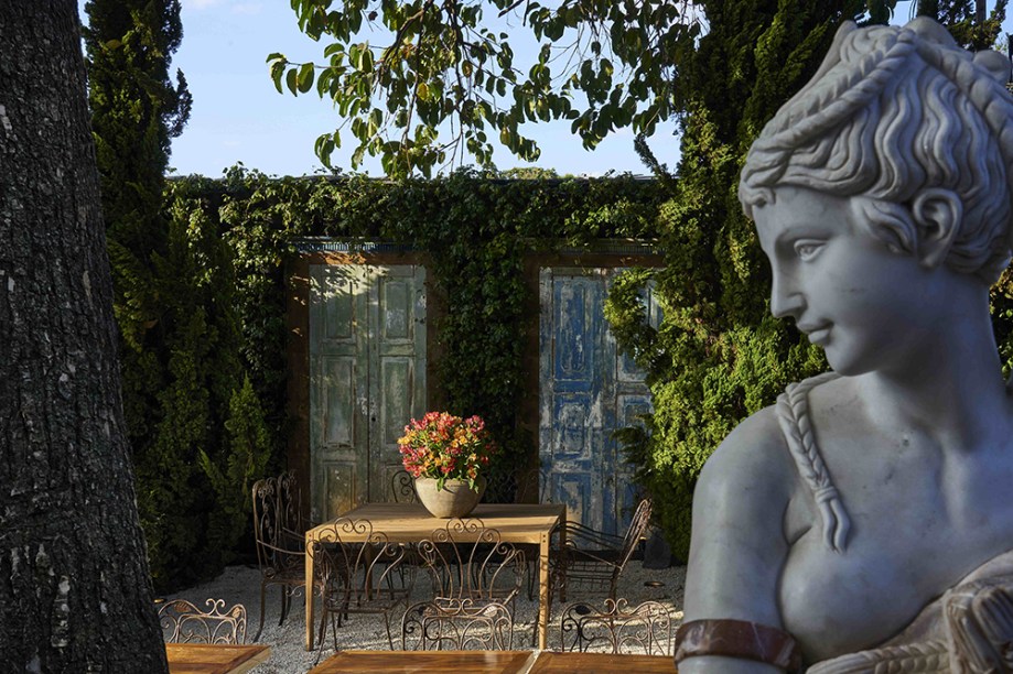 Giardino e espazio di vino - Droysen Tomich, Marcelo Serafim e Flávia Zambelli. O jardim de estilo italiano incorpora o calor dos países mediterrâneos, cercado de muros cobertos de heras e uma escultura do século 18. A ambientação de uma casa antiga é sugerida pelas portas originais de uma fazenda colonial mineira. Uma grande mesa de madeira de demolição, de 4 metros de extensão, é acompanhada de cadeiras de ferro, perfeita para degustar vinhos.