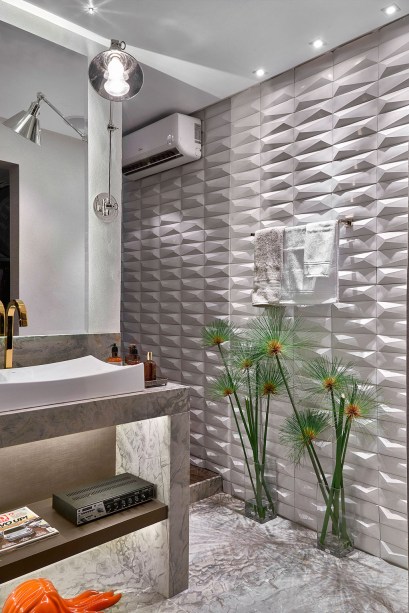 Banho do Rapaz - Wânia Simão - Para dar a impressão de que o ambiente de 7,29m² é maior, a saída foi apostar no branco com uma leitura moderna e na variedade de materiais. Os revestimentos trazem geometrismo e relevo, como o aplicado na parede. O piso recebeu um mármore escovado, que também aparece na bancada da cuba desenhada pela arquiteta. O projeto luminotécnico combina a fibra ótica com efeito de céu estrelado na área da ducha e uma iluminação em cristal que incide na bancada, além da utilização de LEDs, spots e mini-lasers.