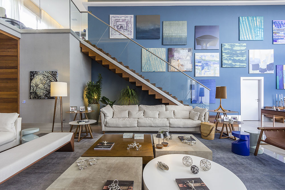 CASACOR Campinas 2016. Living - Daniele Guardini e Adriano Stancati. Sof&aacute;s e Poltronas da Saccaro se destacam a frente da grande parede azul, que abriga a cole&ccedil;&atilde;o de telas assinadas por artistas convidados. A madeira certificada e o porcelanato conferiram praticidade e calor, enquanto o piso cinza deu um toque sofisticado. Repare no conjunto de mesas de centro, de diferentes materiais e formatos.