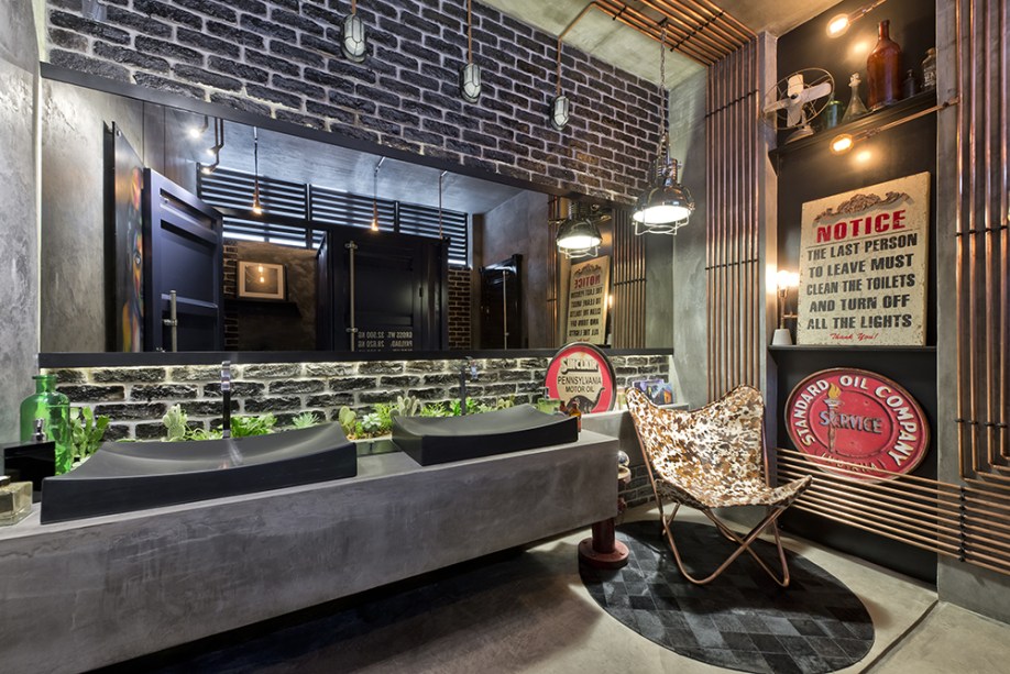 CASACOR Paraná 2016. Lavabo Funcional - Barbara Penha e Pauline Moraes. As cabines do banheiro foram produzidas sob medida e reproduzem a estrutura de um contêiner nas divisórias. A estética industrial dos lofts novaiorquinos prossegue no revestimento de tijolos e nas tubulações e fiações aparentes. O toque final é a poltrona Butterfly, fabricada pela Casalecchi e projetada originalmente em 1938.