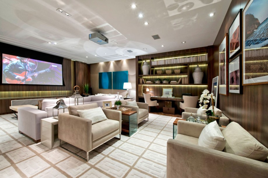 Estar Íntimo. A arquiteta Viviane Loyola criou um ambiente multifuncional que pode ser utilizado como estar íntimo, home office, home theater e living para receber. Móveis fixos e painéis amadeirados envolvem o espaço, que também traz o toque acolhedor de mantas de tricô, peles no puff e nas almofadas. O tapete personalizado foi desenhado pelo escritório da profissional.