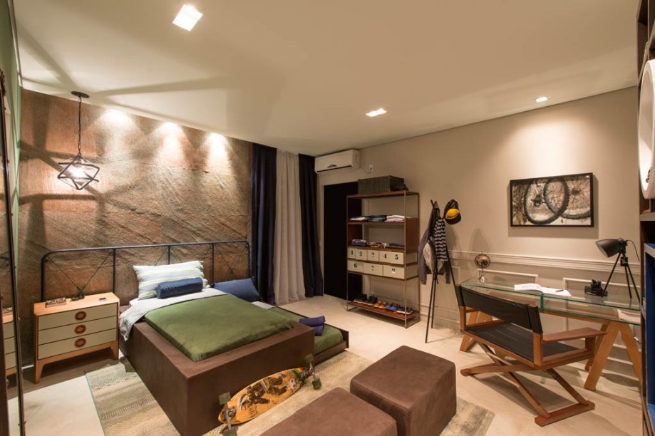 CASACOR Santa Catarina 2015 | Studio do Adolescente - Bruna Dezordi - A arquiteta manteve o concreto aparente no piso e apostou em paredes de tons claros, algumas em pedra. A cama recebeu uma cabeceira em ferro nas cores verde e azul, além de um revestimento estofado em couro marrom. Ela é bem acompanhada pelo criado-mudo, também com acabamento em couro, e pelo pendente em ferro. Quadros da artista Nilza Dezordi, com o tema bicicleta, finalizam.
