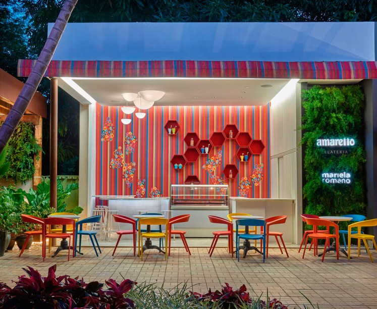Sorveteria - Mariela Romano - Pensado para ser divertido e refrescante, o espaço é definido pelos tecidos coloridos no toldo e nas sobreposições aplicadas às paredes internas. No mobiliário, destaque para as cadeiras e bancos assinados pelo designer Índio da Costa, que exploram a vibrante paleta de cores. O restante é branco, para equilibrar o resultado. O projeto luminotécnico contempla a utilização de luz indireta de sancas, um mix de plafons e iluminação em LED que focaliza os detalhes, além de embutidos de piso e refletores na parte externa.