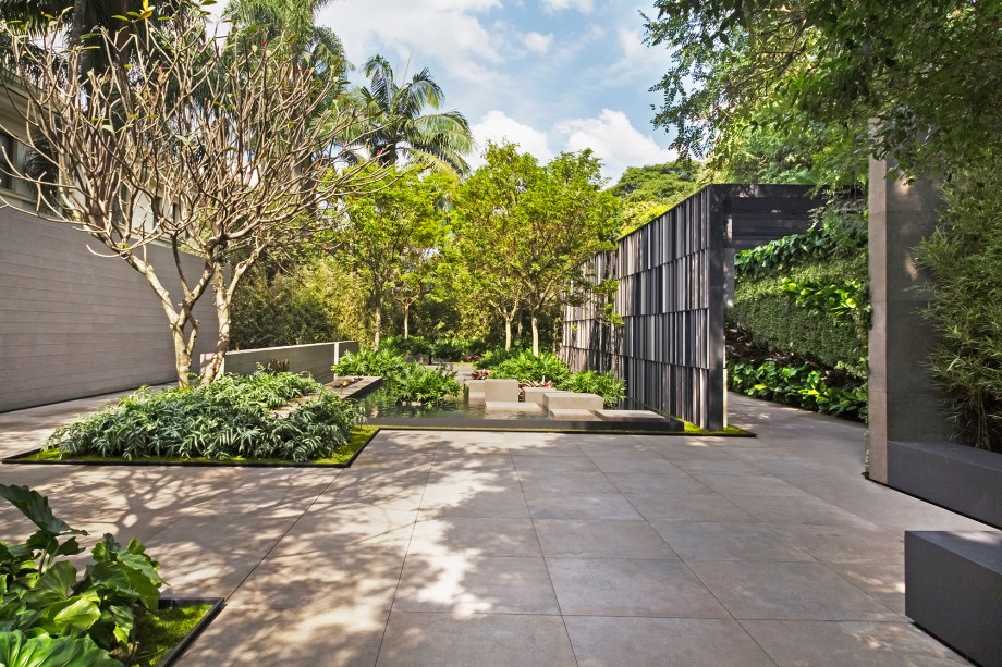 <span>CASACOR São Paulo 2016. Praça Eliane - Alex Hanazaki. O desafio de equilibrar um produto industrializado e a natureza foi respondido com o bom uso de geometrismos. As formas de plantas nativas, como o pau-brasil, dialogam com os porcelanatos em diferentes tons que compõem brises nas laterais, com estruturas metálicas. O caminho flutuante no espelho d’água também foi revestido no material em tom mineral, que contrasta com os seixos negros no fundo.</span>