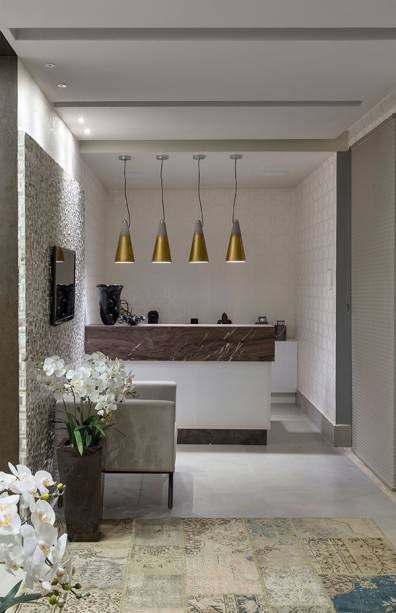 Feitos de concreto, os pendentes Block deste hall de entrada trazem assinatura da Stella Design, e sugerem um contraponto de cor no lugar repleto de tons s&oacute;brios. O tingimento dourado, aferido as pe&ccedil;as posteriormente, emprestou, ainda, eleg&acirc;ncia ao ambiente criado pela arquiteta Josy Brandstetter e o designer de interiores Denis Rezende, na &uacute;ltima edi&ccedil;&atilde;o da CASACOR Goi&aacute;s.