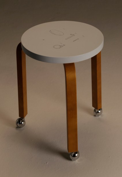 A proposta da artista Gio Soifer de inserir rodas ao desenho original da banqueta é criar não só um possível movimento deste corpo que suporta e é apoio para outro corpo, mas também de pensar na dinâmica do próprio ato de “customizar” um design já consagrado. “O processo é evidenciado quando ilustro no próprio tampo da banqueta o manual original, somado ao desenho das rodas anexadas”, conta Gio.
