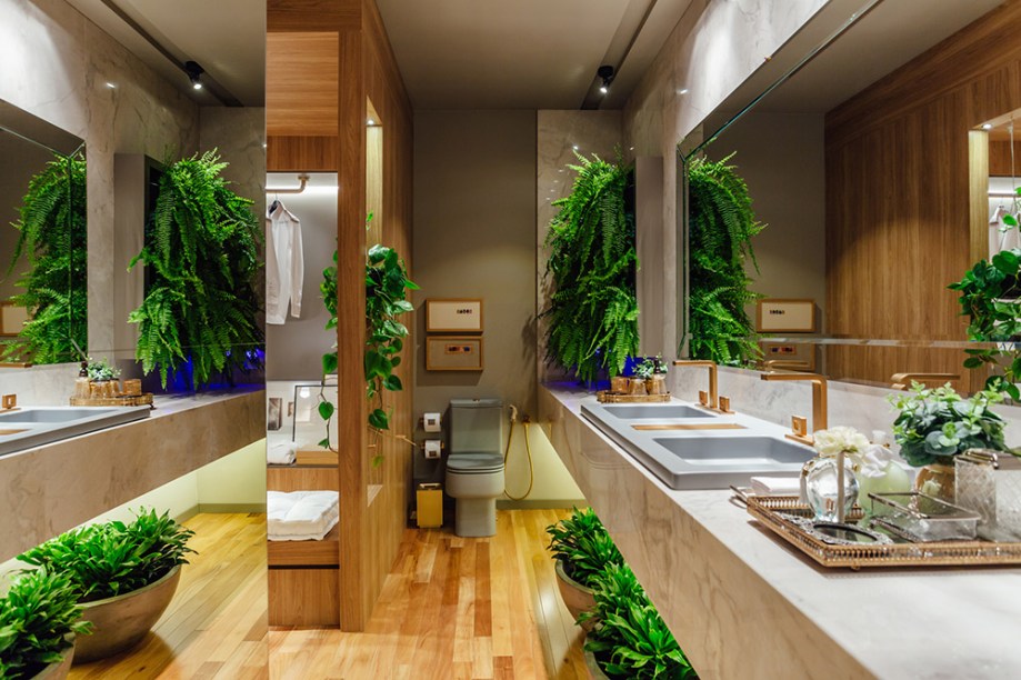 Suíte para Estar - Joana Deicke e Maria Manoela Bento Pereira. A sala de banho integrada ao dormitório e ao estar recebe piso de madeira natural e não abre mão do verde das plantas, para refrescar e colorir. A bancada utiliza mármore branco paraná, enquanto a marcenaria foi executada em melamina carvalho hanover.