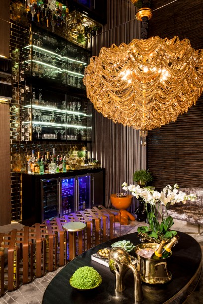 Home Bar - Flávio Moura. O bar acolhedor abusa de elementos clássicos como o piso de mármore exótico nos tons de cinza com veios dourados, as paredes revestidas com réguas de madeira natural e tijolinhos de cerâmica. A iluminação indireta cria a sensação de aconchego.