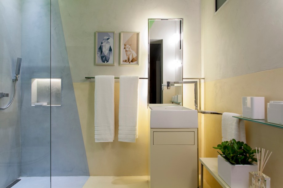 Banheiro dos Filhos - Pedro Andrade e Sara Bezerra. O espaço incorpora o conceito do Color Blocking, que combina harmonicamente cores opostas no círculo cromático. Através das cores aplicadas no microcimento pigmentado, um material resistente às áreas molhadas, os profissionais quebraram os limites dos planos (piso, paredes e teto). Os elementos metálicos e o espelho auxiliam na ampliação do ambiente.
