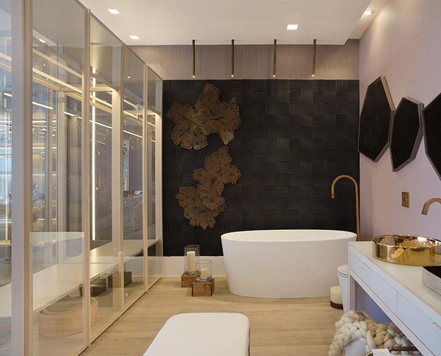 Loft da Executiva – Claudia Pimenta e Patricia Franco. Pensando em uma empresária com alma cosmopolita as profissionais criaram esse elegante espaço. Na paleta de cores predomina o pink millennial, um tom de rosa nude. Móveis cheios de personalidade, como o sofá em linhão branco curvo e estantes e armários de vidro, preenchem o ambiente. A transparência dos armários é utilizada para separar o banheiro do espaço.