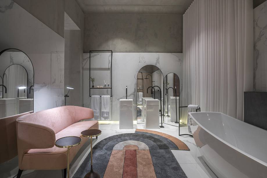 CASACOR Minas Gerais: Sala de Banho - Rodrigo Aguiar. O revestimento que remete ao mármore carrara e as formas de arcos não deixam dúvidas quanto ao desejo de nobreza. O sofá curvo é ultraconfortável e conversa com o desenho retrô do tapete. Repare também na iluminação que vem dos rodapés suspensos.