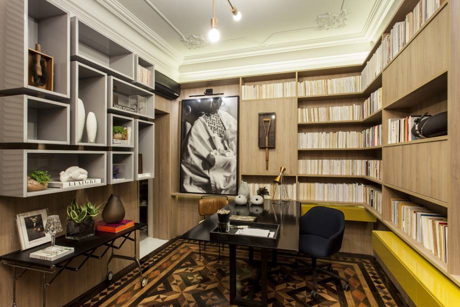 CASACOR Bahia: Escritório da Casa - Eliane e Laís Kruschewsky. Os profissionais mantiveram as características originais da casa, misturando os estilos com uma decoração contemporânea inserida num contexto arquitetônico clássico. O piso original em parquet, a esquadria e detalhes de gesso no teto foram aproveitados. Os tons neutros e escuros, como cinza e preto, além da utilização de materiais como laca, ferro pintado, cobre e couro reforçam o conceito do ambiente