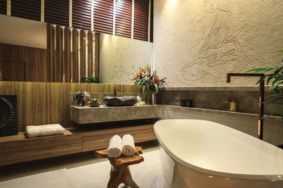 CASACOR PR: SPA em Casa - Katleen Luizaga. As paredes recebem painéis madeirados em louro freijó e uma textura assinada pela artista Marilene Ropelato, com o toque tailandês desejado pela profissional. A banheira de imersão Amiata, em rocha vulcânica e resina de alta performance, mantém a temperatura da água por mais tempo. A linha de metais é a Gold, da Deca.