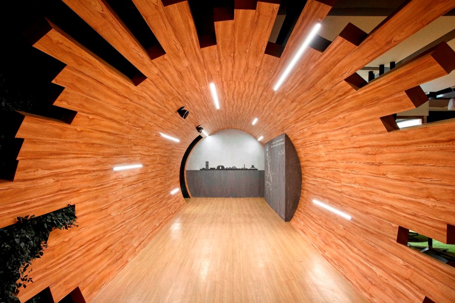 Espaço do Empreendedor – Sérgio Borges. O arquiteto é um estudioso da neuroarquitetura e preparou uma experiência inusitada. Antes de adentrar no espaço em si, o visitante percorre o túnel de sete metros, revestido com duas tonalidades de madeira em réguas descontínuas. A iluminação traz um apelo gráfico e cria interferências na superfície.