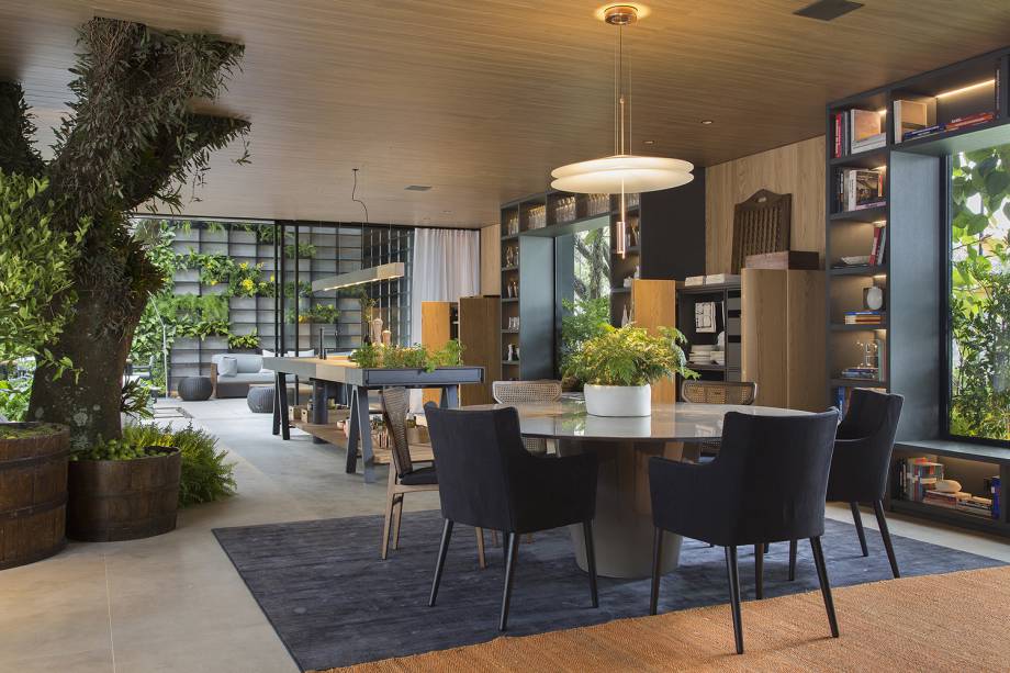 Casa Terra - Paola Ribeiro. Duas grandes árvores que se encontravam no terreno foram integradas ao espaço. A sensação de estar em um jardim é reforçada pelo uso de vidro e grandes caixilhos, convidando o verde para a ambientação em tons naturais e amadeirados.