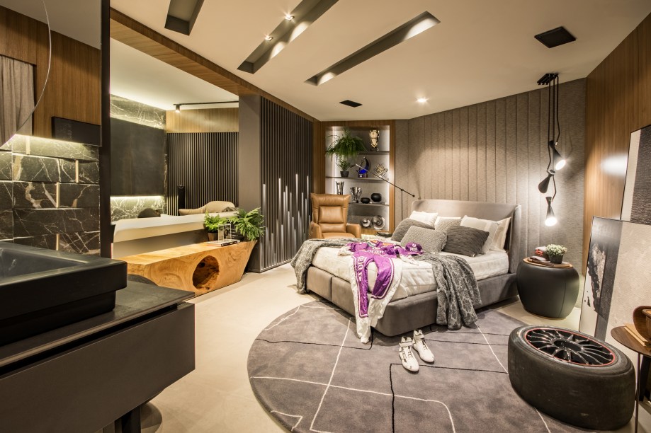 CASACOR Paraná 2019. Loft do Piloto - Priscila Ruon e Suely Ruon. Living, espaço gourmet, quarto, closet e sala de banho são distribuídos nestes 78 m². O universo automobilístico levou à escolha dos tons de cinza em vários materiais do projeto, suavizados pela presença dos amadeirados e do couro. Entre as peças de design, itens assinados por Paulo Alves e Rejane Carvalho Leite. A cama e os estofados são da marca italiana Natuzzi.