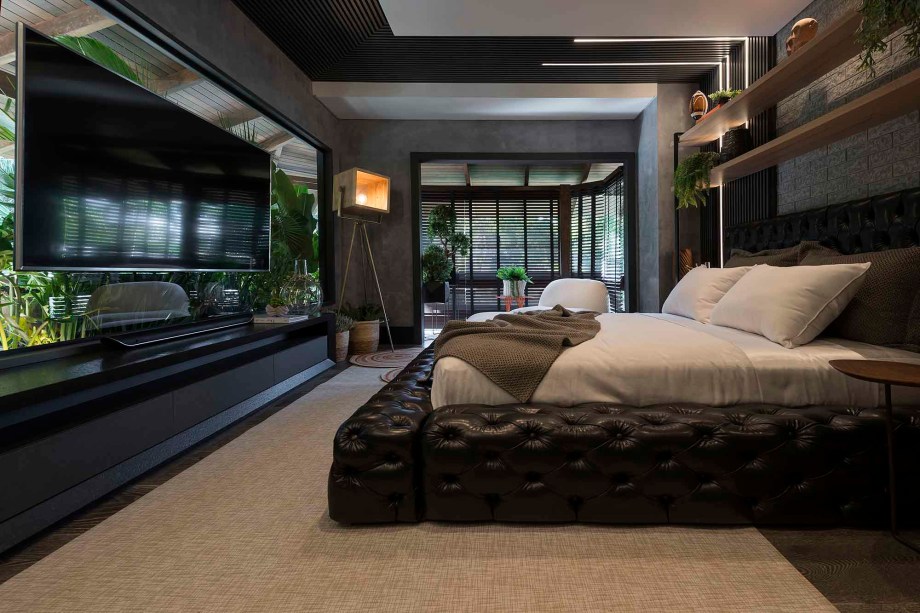O ambiente de 32 m² projetado para um casal jovem contrata a urbanidade, marcada pelos tons escuros dos revestimentos, e a natureza, que adentra pelo vidro no qual a TV foi suspensa. O projeto Suíte do Casal também traz a textura marcante da pedra, no mesmo tom do concreto. Suíte do casal - Mariane Bassegio e Nando Machado - CASACOR Bálneario Camboriú 2019.