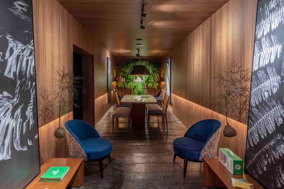 Espaço Comercial (Fibraplac) - Helade Lorenzoni. Ponto de descanso, área de selfie e a arquitetura contemporânea com referências ao Art Déco oferecem ao visitante uma experiência agradável com a marca. O ambiente foi desenvolvido no interior da caixa de MDF no padrão Nogueira, enquanto o piso reaproveita madeira de demolição. As fotografias em grande formato são de Fabio Petry.