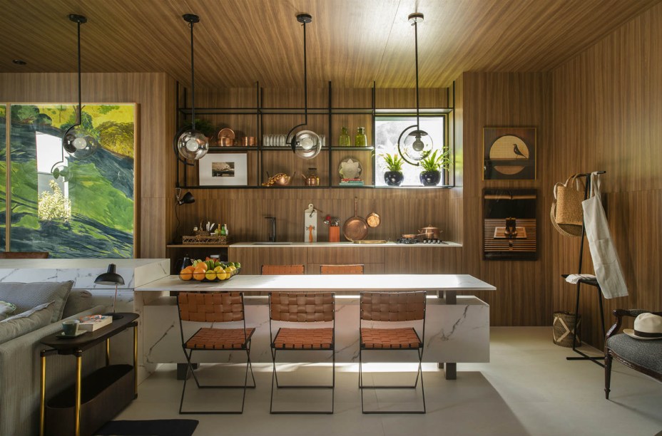 Dulce de Figueiredo Ferraz e Thácia Balbão - Loft Refúgio Urbano. Um ambiente que dá vontade de entrar e ficar. Com essa energia, a dupla projetou uma casa de verdade, para ser vivida, com passado, presente e futuro. Quente e acolhedor, o lar é abraçado pela madeira, deixando a bancada da pia e a torre de eletrodomésticos quase imperceptíveis. A mesa com base em mármore é uma extensão do aparador atrás do sofá, conectando os ambientes. A iluminação vem na medida, com peças do alemão Ingo Maurer.