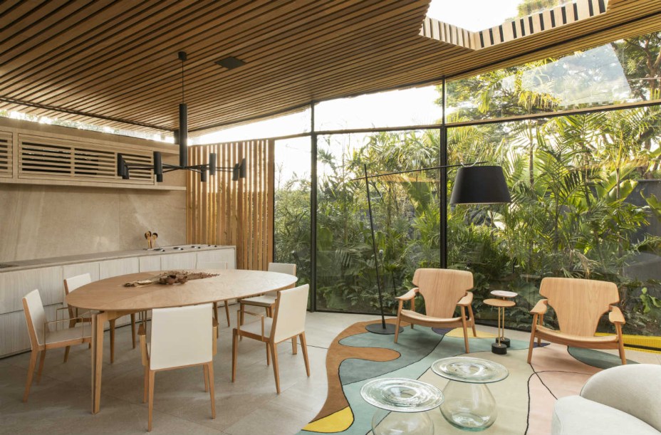 Mariana Orsi - Loft DECA. Os 56 m² se expandem e adquirem a dimensão do jardim que adentra o espaço integrado. Painéis de vidro são responsáveis pelo fechamento, enquanto o teto, recortado por algumas aberturas, é revestido de Tauari maciço. Um material que remete a uma casa de palafitas. As poltronas Diz são de Sergio Rodrigues.