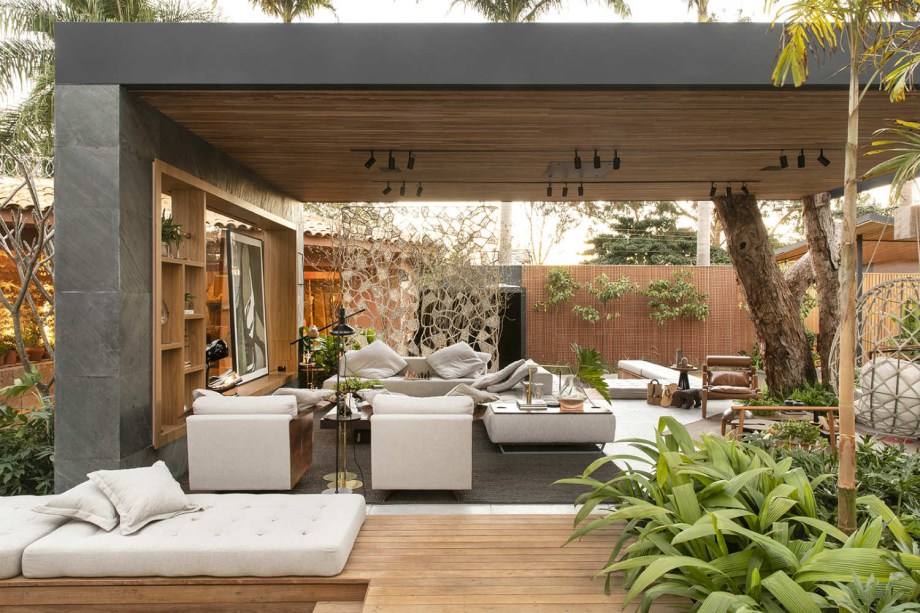 Roberta Alonso e Mariana Oliveira - Welness Lounge. O uso combinado da estrutura metálica com o concreto e a madeira define o espaço. Um enorme galho, inclusive, foi reaproveitado para dar sustentação à cobertura. Com vocação multiúso, o ambiente reúne poltronas e estofados variados, iluminação versátil em trilhos e um layout fluido. Sem barreiras visuais, a conexão com a natureza é total.