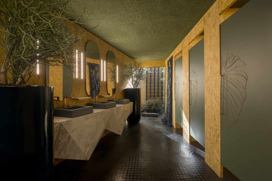Banheiro Cabana Verde - Suellen Paul. O próprio nome reafirma seu compromisso ecológico: a cabana se desenrola em forte ligação com a natureza, seus materiais e seus contornos. A revitalização de materiais reciclados é provavelmente seu maior acerto. Assim, lixos encontrados na praia, como plásticos, canudos, sacolas e tampinhas se transformam em objeto de design, como possível observar no painel trançado ao fundo da foto.