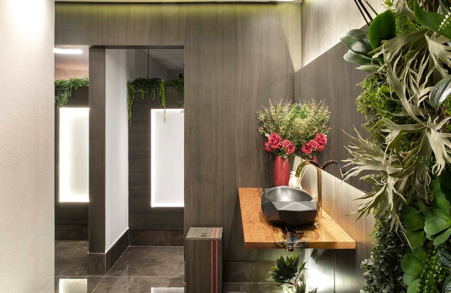 CASACOR Espírito Santo 2019. Lavabos Funcionais - Aline Ane, Aline Fialho e Aline Rita Laureano. O espaço tem 28,50 m² e traz uma dimensão inclusiva, para atender do bebê ao idoso. A natureza se expressa no uso de vegetação e na madeira reaproveitada da bancada, com acabamento em resina, despertando a consciência da preservação do planeta. Lâmpadas de LED e peças redutoras de consumo de água também promovem um pensar sustentável.