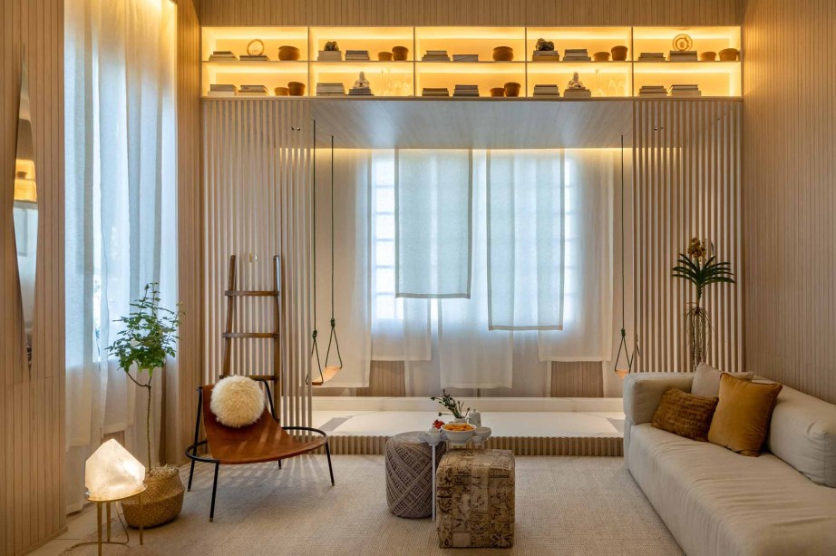 CASACOR Rio de Janeiro 2019. Bianca da Hora - Sala Shanti. Minimalista, o espaço combina o acolhimento da madeira, a leveza dos tecidos naturais e a funcionalidade no mobiliário de jovens designers brasileiros. Na janela, o fechamento ganha uma sobreposição que deixam a claridade fluir. O ripado é outro elemento permeável, utilizado nas laterais do espaço. Os balanços colaboram para a atmosfera lúdica, aconchegante e romântica.
