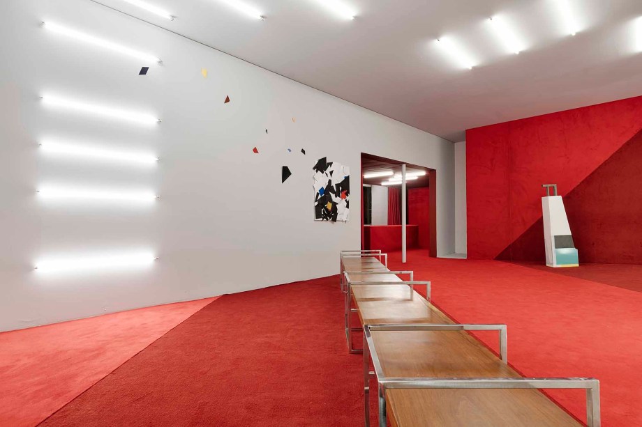 Juliana Vasconcelos - Bilheteria. Com inspiração minimalista e gráfica, a bilheteria se vale de poucos materiais no projeto. No foyer, dois tons de vermelho com paginação em diagonal tingem paredes e balcão. O desenho cria pontos de fuga, direcionando o olhar. A mesma linguagem está na iluminação, mínima: lâmpadas tubulares em LED fazem o caminho no teto e descem pela parede que não foi revestida, que reforça o apelo dramático de vermelho.