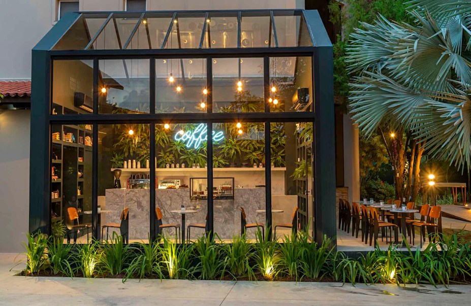 Coffetown – TRPC Arquitetos. Em meio ao Jardim das Delícias, a TRPC Arquitetos assina seu segundo ambiente na CASACOR Bahia 2019. O espaço envidraçado sobre uma leve estrutura metálica traduz o desejo de plena integração do charmoso ambiente corporativo ao verde exuberante do paisagismo local. Projetado para replicar o traço do projeto original da cafeteria Coffeetown, o ambiente permite experimentar plenamente as delícias de um café sofisticado e elegante.