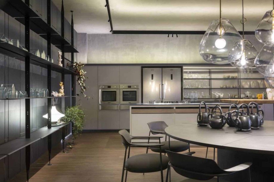 CASACOR Brasília 2019. Walléria Teixeira - Cozinha DECA. Divididos em espaço gourmet e sala de estar, os 100 m² refletem uma linguagem moderna e de inspiração minimalista. Por meio do essencial, promove a interação física e emocional com o público. O cinza se estende do piso de madeira às paredes, formando a base leve e acolhedora do espaço, junto com outras texturas, como linho e couro. Em primeiro plano, o pendente Mush é do designer Jader Almeida.