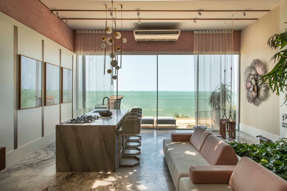 CASACOR Espírito Santo 2019. Estúdio da Árvore Placas do Brasil - Max Mello. Nestes 120 m² foi criado um coworking com mesa de reunião, estações de trabalho, um estar casual, pequena cozinha e uma varanda que se abre para o mar da Ilha do Boi. Grandes aberturas e o teto de vidro garantem a conexão visual com a natureza. A bela castanheira não só foi mantida como fornece sombra e funciona como um eixo importante, com um sofá a seus pés.