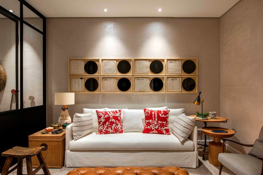 O estúdio de 29m² é aconchegante e explora texturas de materiais naturais como madeira, palha, junco, linho, kilim e couro.  Os vinis aparecem emoldurados atrás do sofá confortável, que foram combinados com peças de antiquário e outras modernas, como as luminárias e mesas laterais. Destaque para o rack vermelho, que leva vida ao lugar. Casa de Verdade - Marcela Pepe - CASACOR São Paulo 2019.
