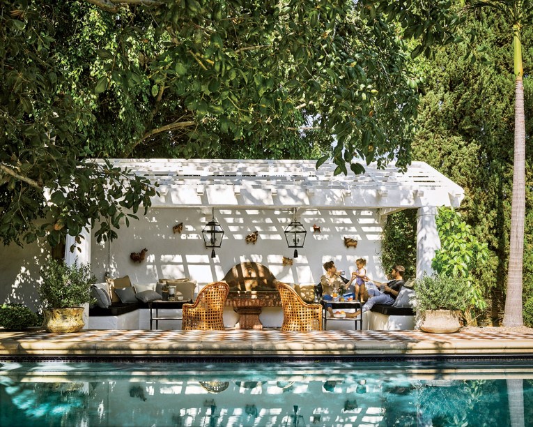 A dupla de designers Nate Berkus e Jeremiah Brent criaram esta piscina para sua residência em Los Angeles. A estrutura foi pintada no alabastro de Benjamin Moore; suas luzes pendentes foram fornecidas pela RH. Quanto aos móveis, as cadeiras são achados vintage de Kreiss e a variedade de travesseiros é da Pottery Barn.