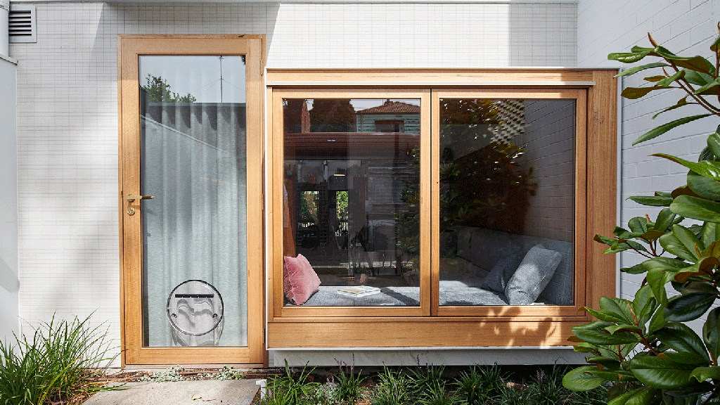 casa-australiana-com-mobilia-embutida-casacor-1 Porta para o quinta vista de fora, um gif com as janelas de vidro e moldura de madeira abrindo. À esquerda, a porta de vidro com moldura em madeira e uma porta redonda para cachorro coberta com uma cortina interna.