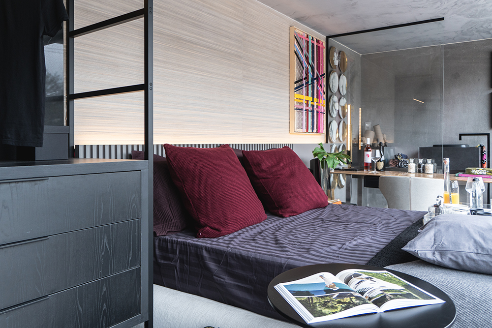 suite-eingen-desafio-janelas-arthur-guimaraes-04 Suíte com cama de casal em primeiro plano, mesa de trabalho e banheiro ao fundo